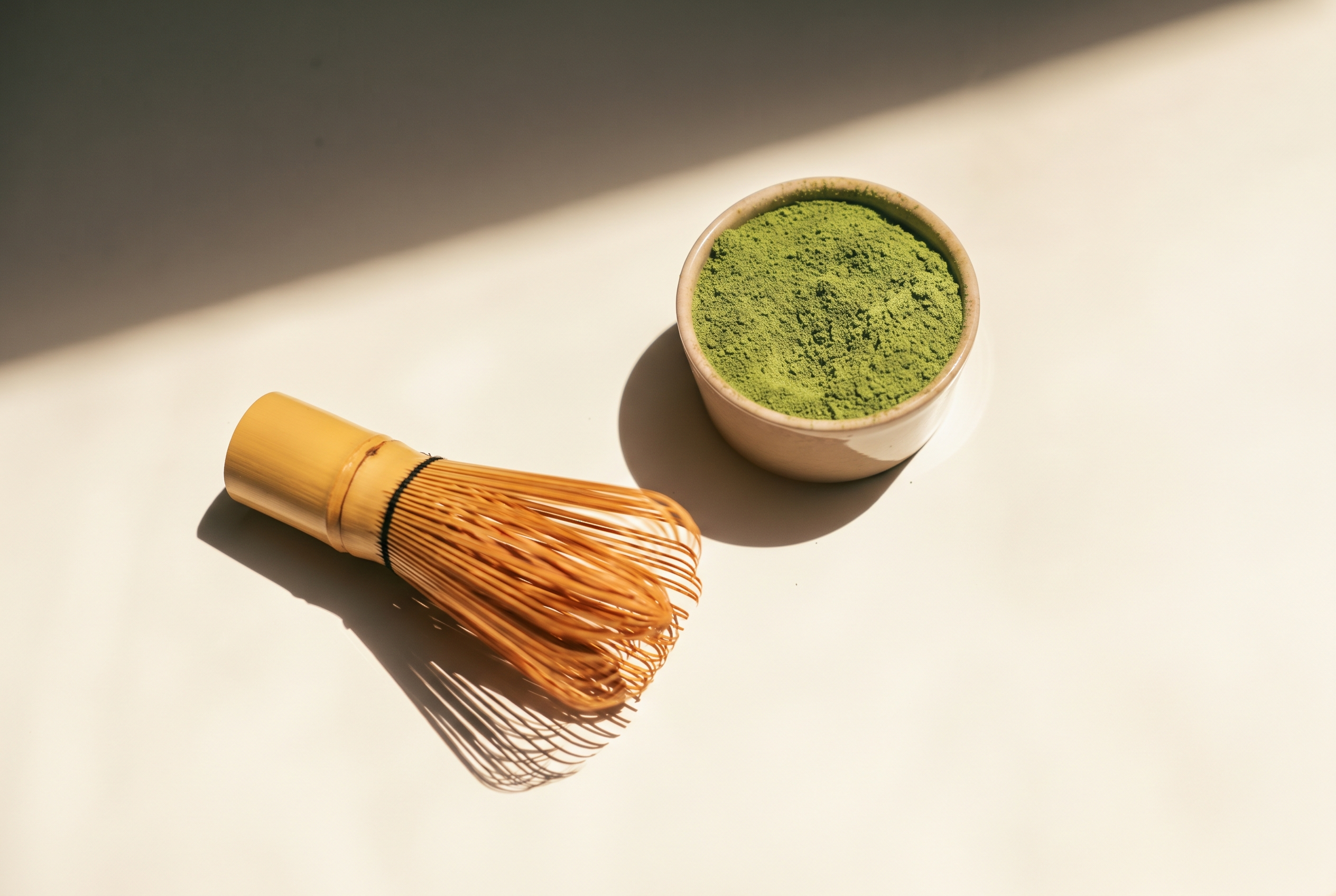 Matcha y batidor de bambú sobre una mesa iluminada por el sol